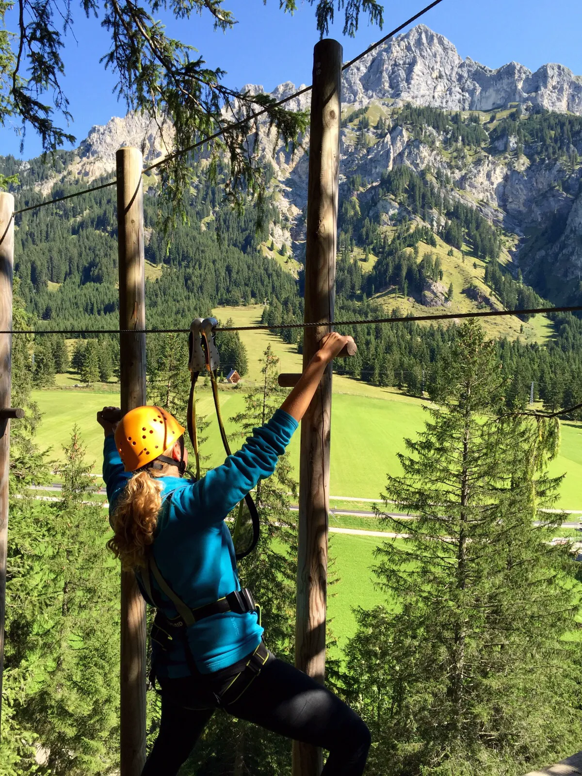 Climber navigating a high-rope element in the Kletterwald Tannheimer Tal with limestone peaks in background